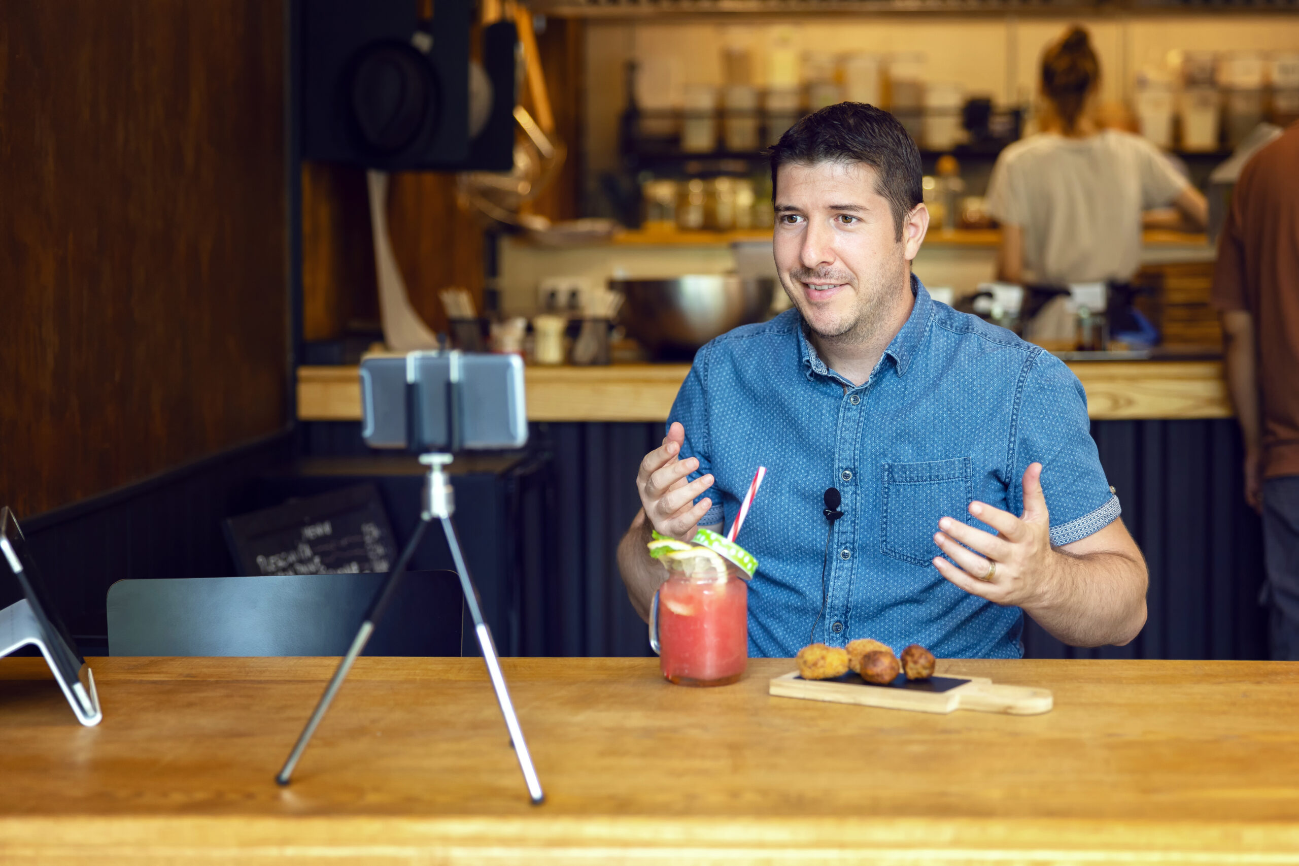 Social media influencer or food blogger creating content inside small restaurant – man sharing online food review using smartphone on tripod and lavalier, smiling content creator vlogger filming video